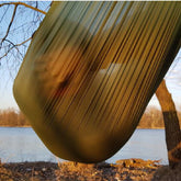 Bushmen ULTRALIGHT Hammock in dark olive color hanging by the river, showcasing its lightweight and strong design.